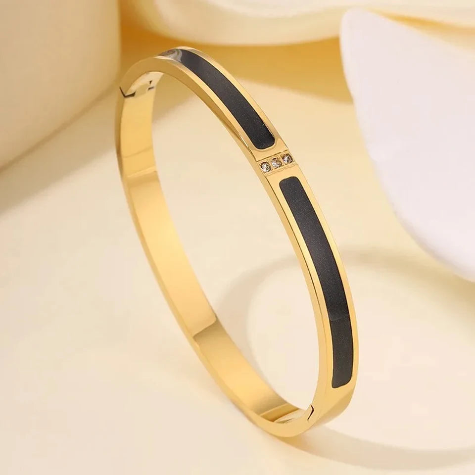 Gold bracelet with black inlay on a soft beige background