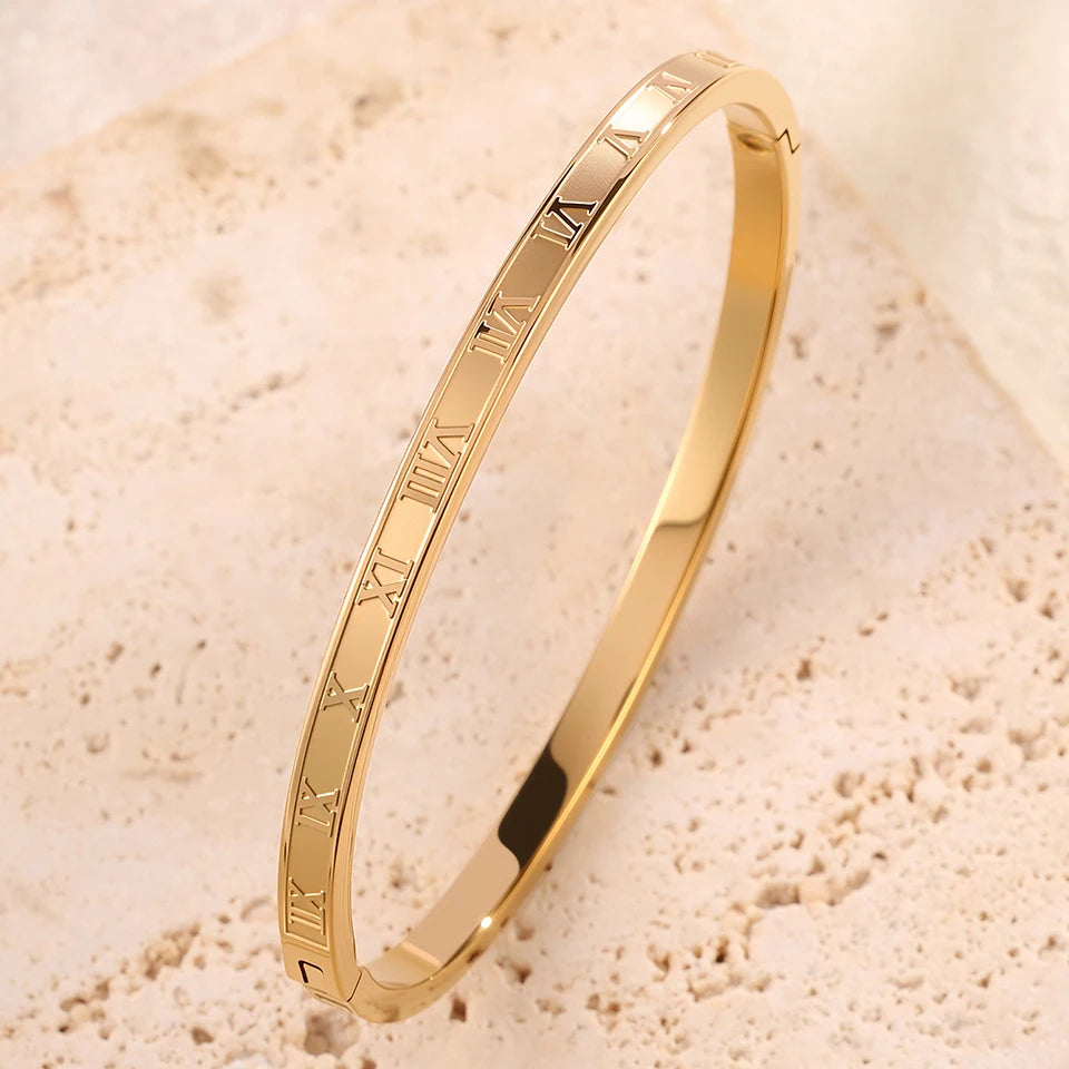 Gold bracelet with Roman numeral design on a beige sandstone background