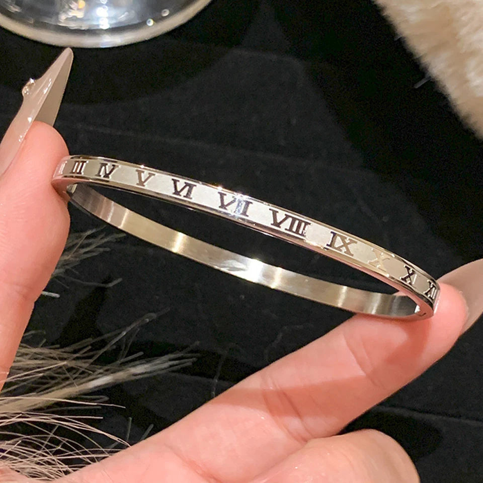Silver bracelet with Roman numeral design held by a hand against a dark background