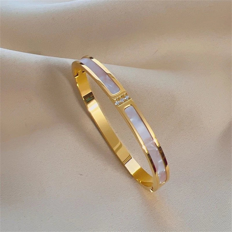 Gold bracelet with a central pearl-like stone on a beige fabric background